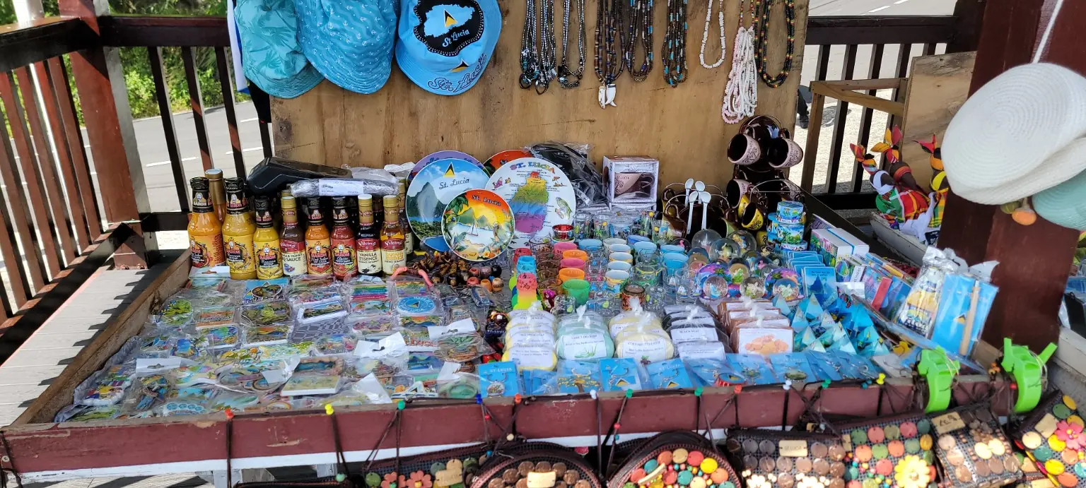 A vendor’s table displays souvenir plates, mugs, packaged goods and bottled sauces beneath hanging hats and necklaces.