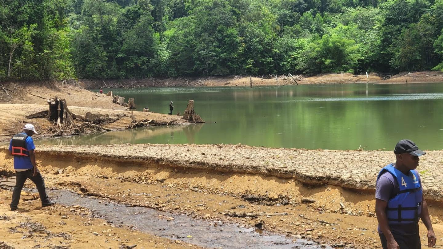 People beside the John Compton Dam reservoir among exposed banks and tree stumps